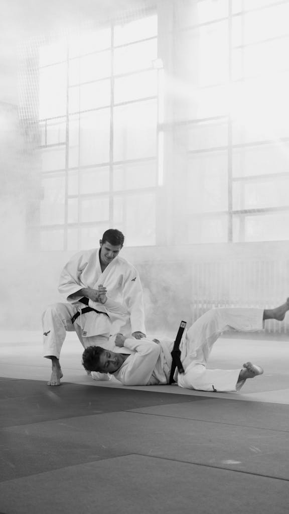 Two martial artists practicing judo in a misty indoor setting, displaying skill and intensity.